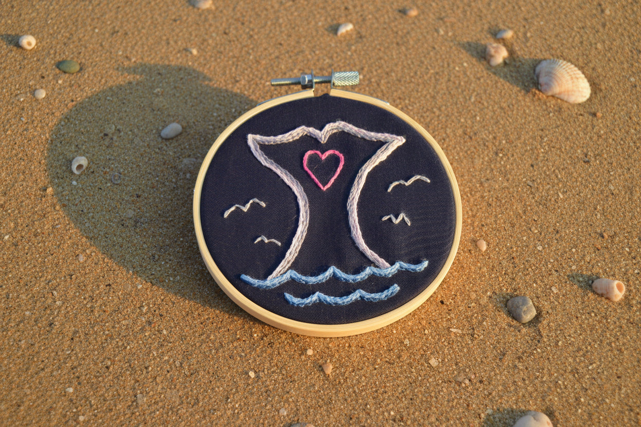 Embroidery hoop with embroidered design of a whale's tail with a heart.